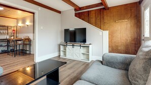 A living room with a flat-screen TV, a grey sofa, wooden floors, and a staircase with wooden paneling. - Warren County Launchpad: Pet-friendly Lebanon Apt (South Lebanon)