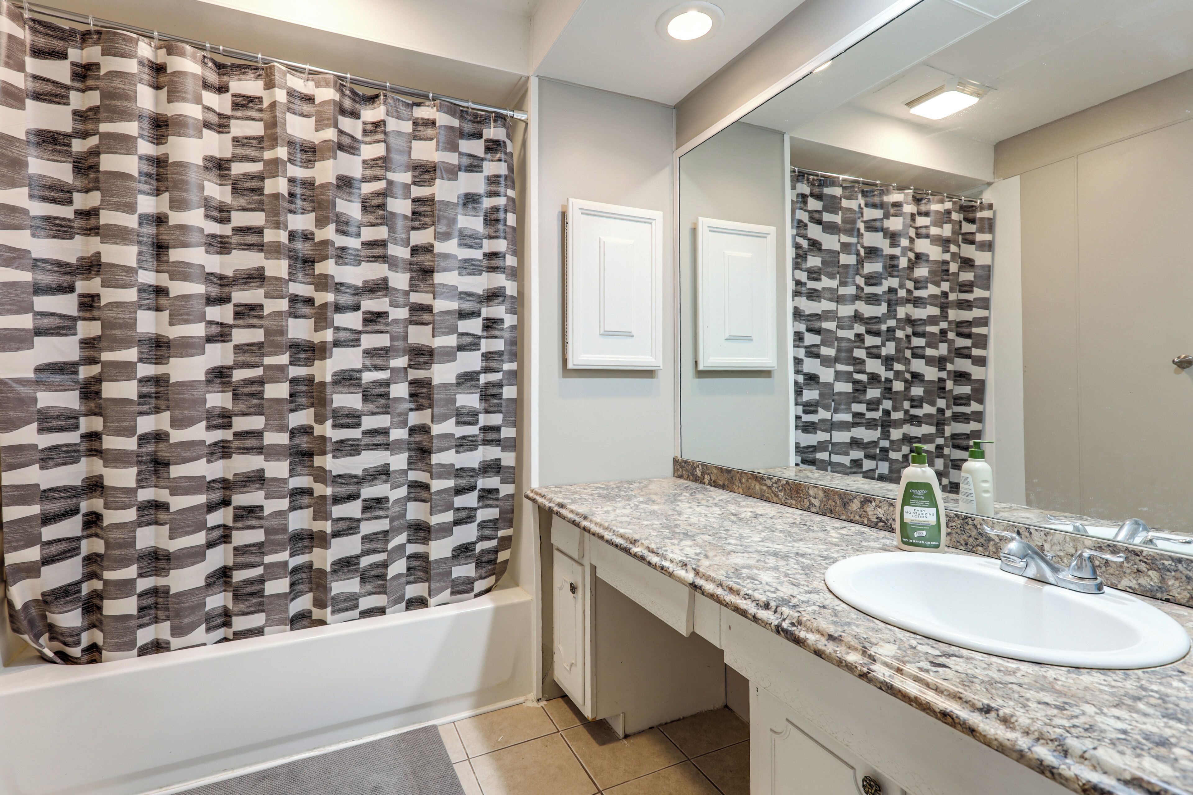 A bathroom with a patterned shower curtain, a sink, a mirror, and a tiled floor.