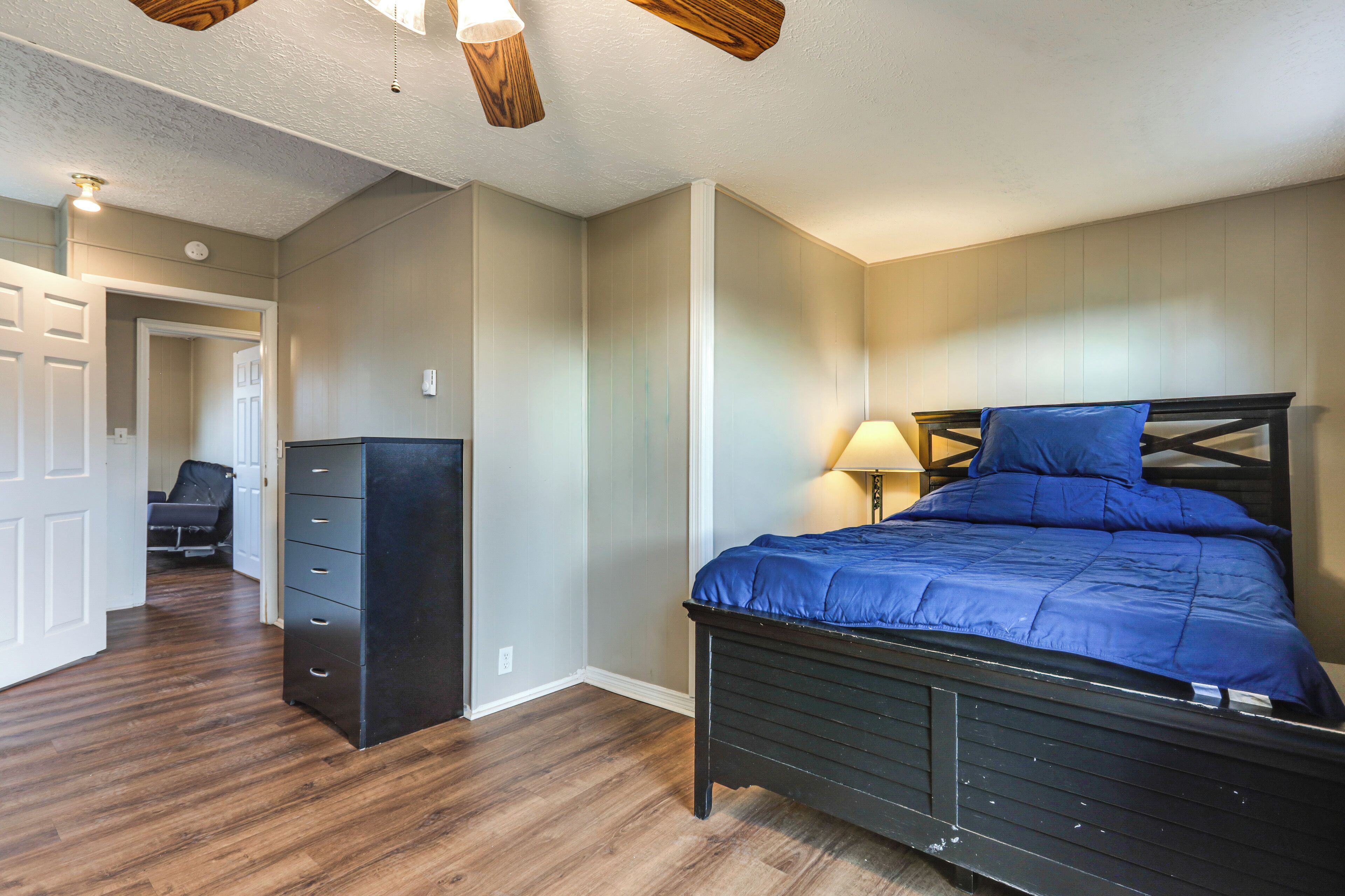 A bedroom with a bed, dresser, and a door leading to another room.