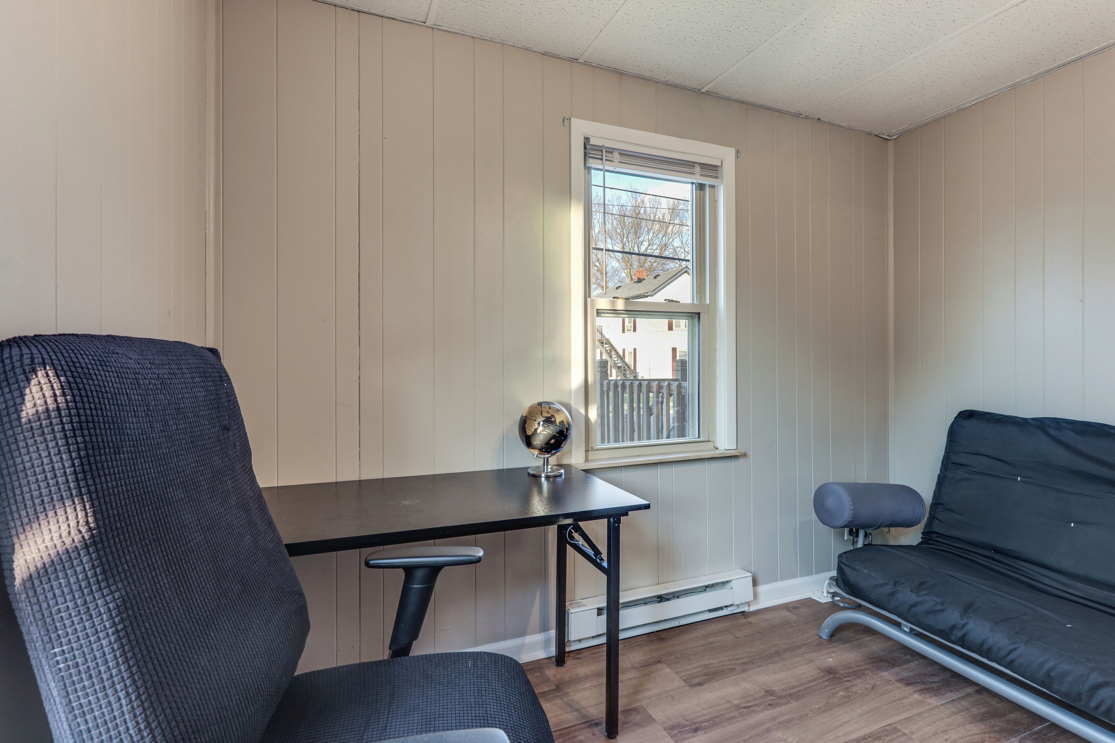 A room with a desk, chair, sofa, and a window with a view of a building.
