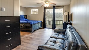 A bedroom with a bed, a dresser, a leather sofa, a ceiling fan, and a window with curtains. - Warren County Launchpad: Pet-friendly Lebanon Apt (South Lebanon)