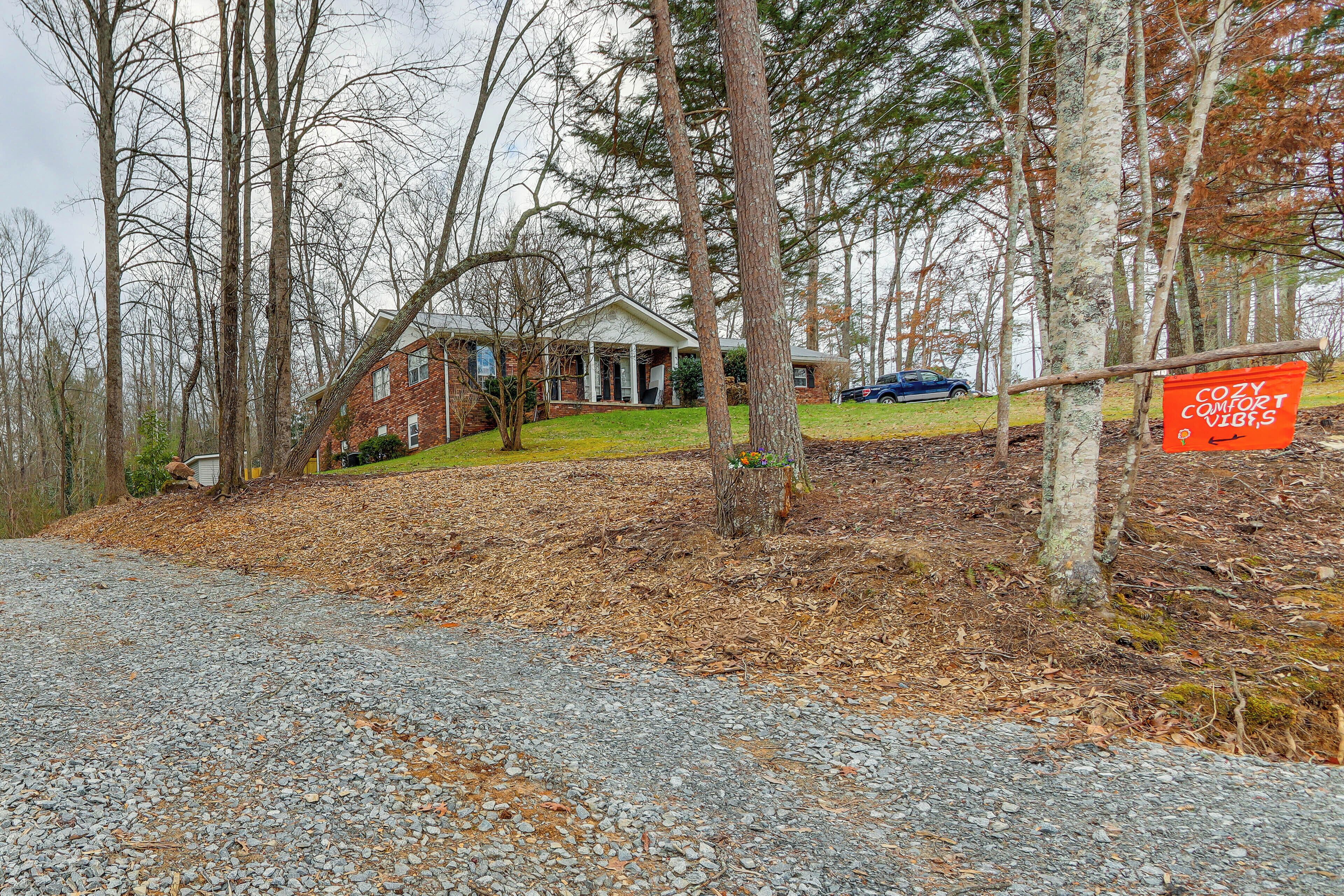 A house with a porch, surrounded by trees and a gravel driveway.