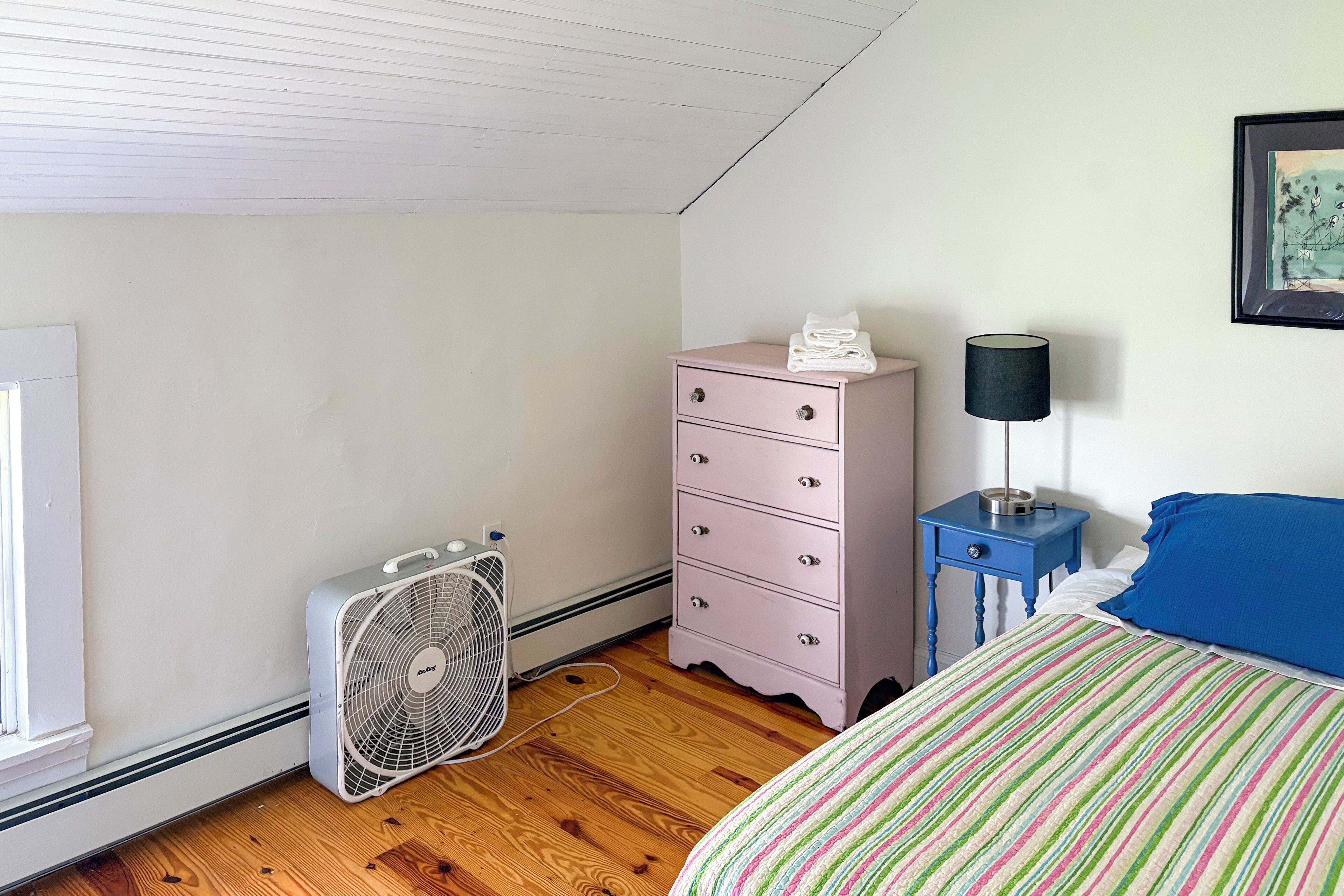 Une chambre à coucher avec un lit, une commode, un ventilateur et une lampe.