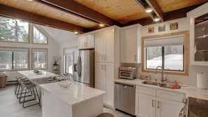 A modern kitchen with a central island, stainless steel appliances, and large windows. - 5 Mi to Soda Springs Mtn Resort: Forest-view Gem! (Truckee)