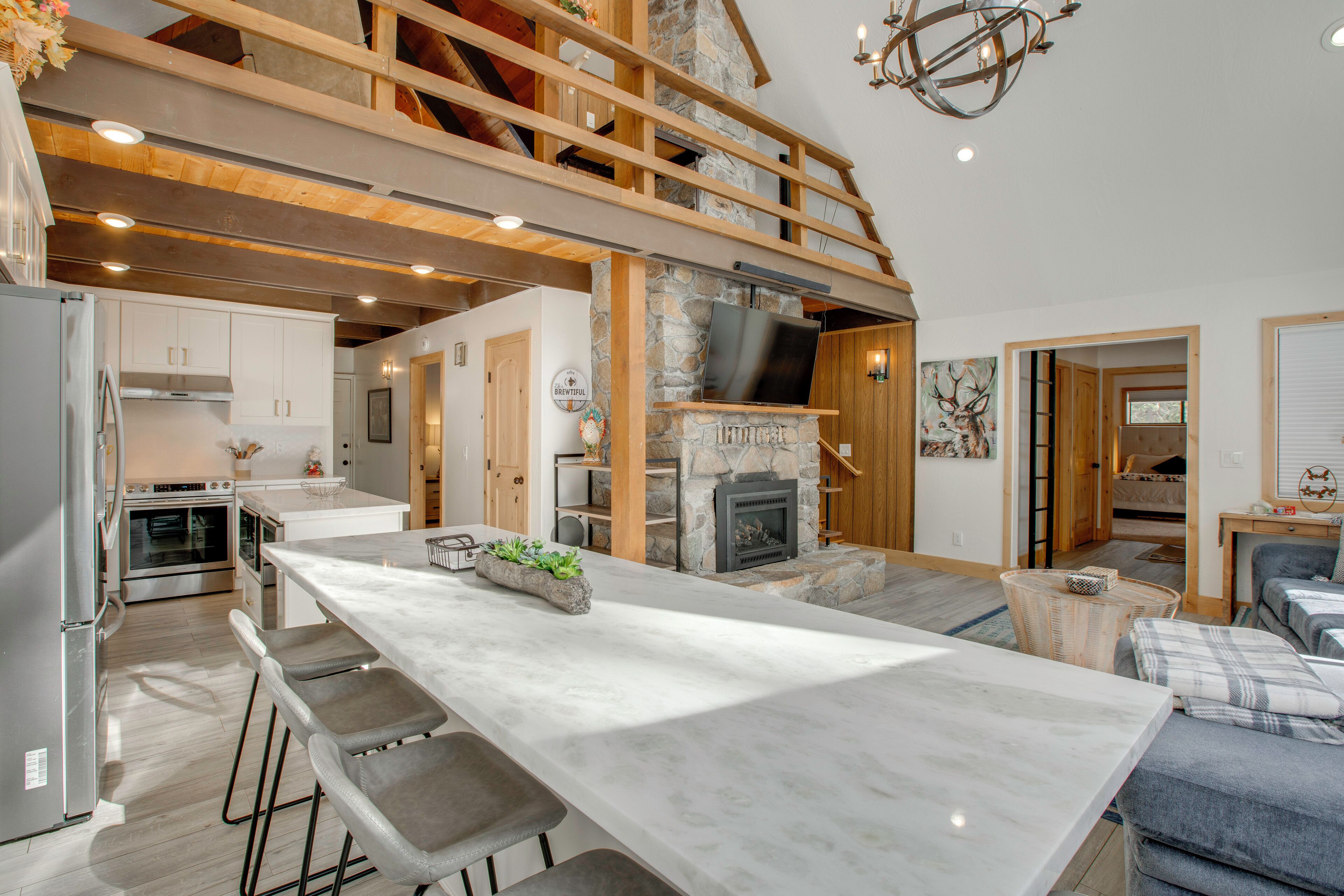 A spacious kitchen with a large island, a stone fireplace, and a loft area with wooden beams.