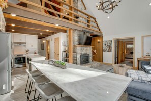 A spacious kitchen with a large island, a stone fireplace, and a loft area with wooden beams. - 5 Mi to Soda Springs Mtn Resort: Forest-view Gem! (Truckee)