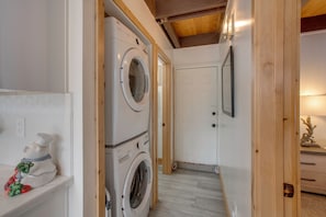 A laundry room with stacked washing machines, a white door, and a wooden ceiling. - 5 Mi to Soda Springs Mtn Resort: Forest-view Gem! (Truckee)
