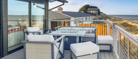 A deck with outdoor furniture, a fire pit, and a view of the beach.
