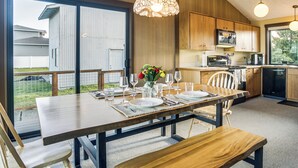 Un comedor con mesa de madera dispuesta para cuatro, un banco y vista al patio trasero a través de amplios puertas correderas.