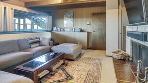 Una sala de estar con sofá, reposapiés, mesa de centro, chimenea y estantería.