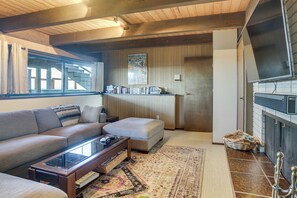 A living room with a sofa, ottoman, coffee table, fireplace, and a bookshelf. - Sequim Shoreline Retreat w/ 2 Decks: Dogs Welcome! (Sequim)