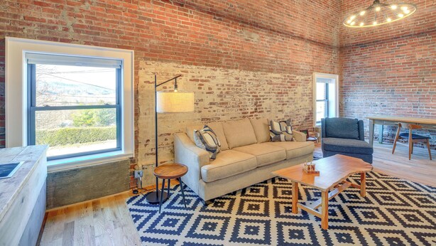 A room with a brick wall, a sofa, a lamp, a table, and a patterned rug.