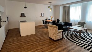 A modern living room with a sofa, armchair, coffee table, and a dining area with chairs and a table.