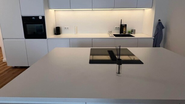 A modern kitchen with white cabinetry, a built-in oven, a black range hood, and a minimalist countertop.