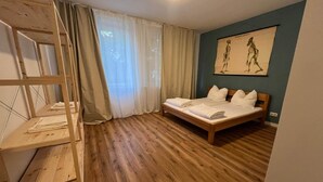 A bedroom with a bunk bed, a bed with pillows, a wooden floor, a window with curtains, and a wall with a skeleton illustration.