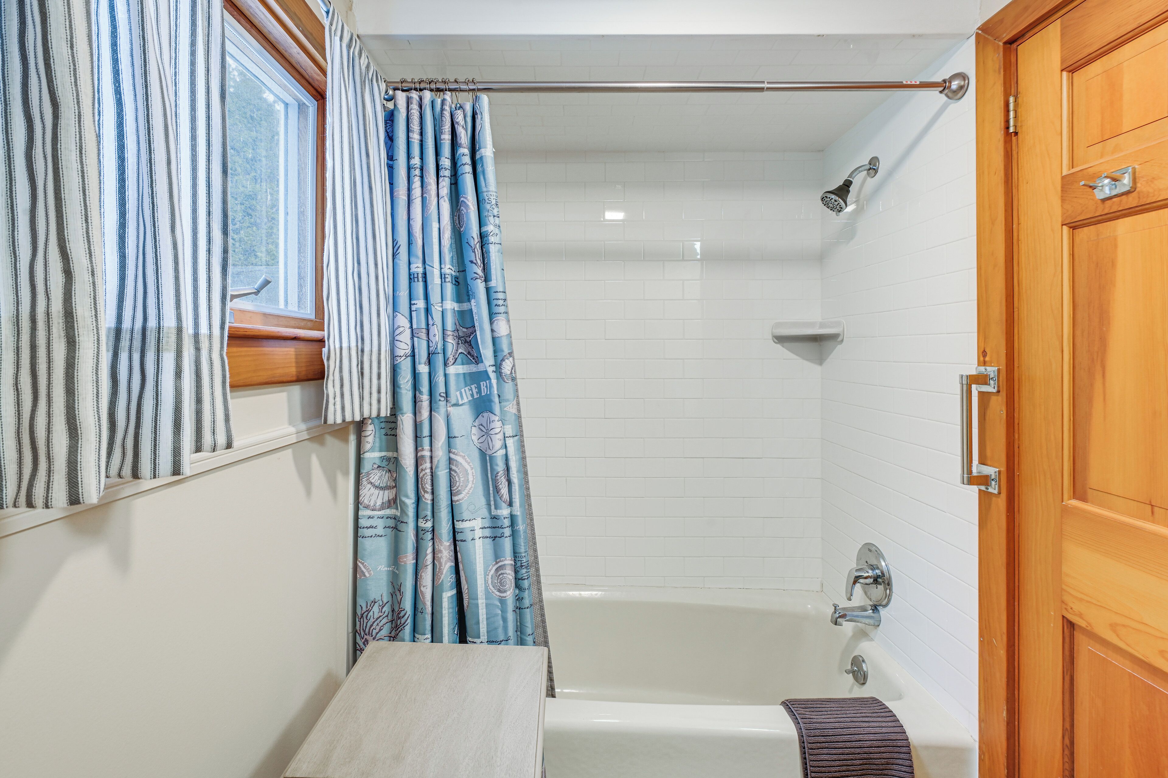 A bathroom with a bathtub, a shower, a wooden door, and a window with curtains.