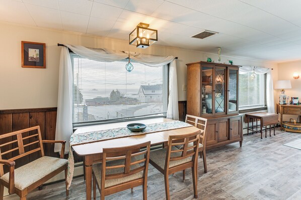 A dining area with a wooden table, chairs, a cabinet, and a window with blinds. - Walk to Pigeon Hill Bay: Coastal Maine Cottage (Steuben)