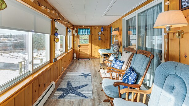A wooden interior with a view of the outdoors, a star-patterned rug, and a seating area with chairs and a table. - Walk to Pigeon Hill Bay: Coastal Maine Cottage (Steuben)