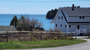 A house with a porch, a view of the ocean, and a fenced yard. - Walk to Pigeon Hill Bay: Coastal Maine Cottage (Steuben)