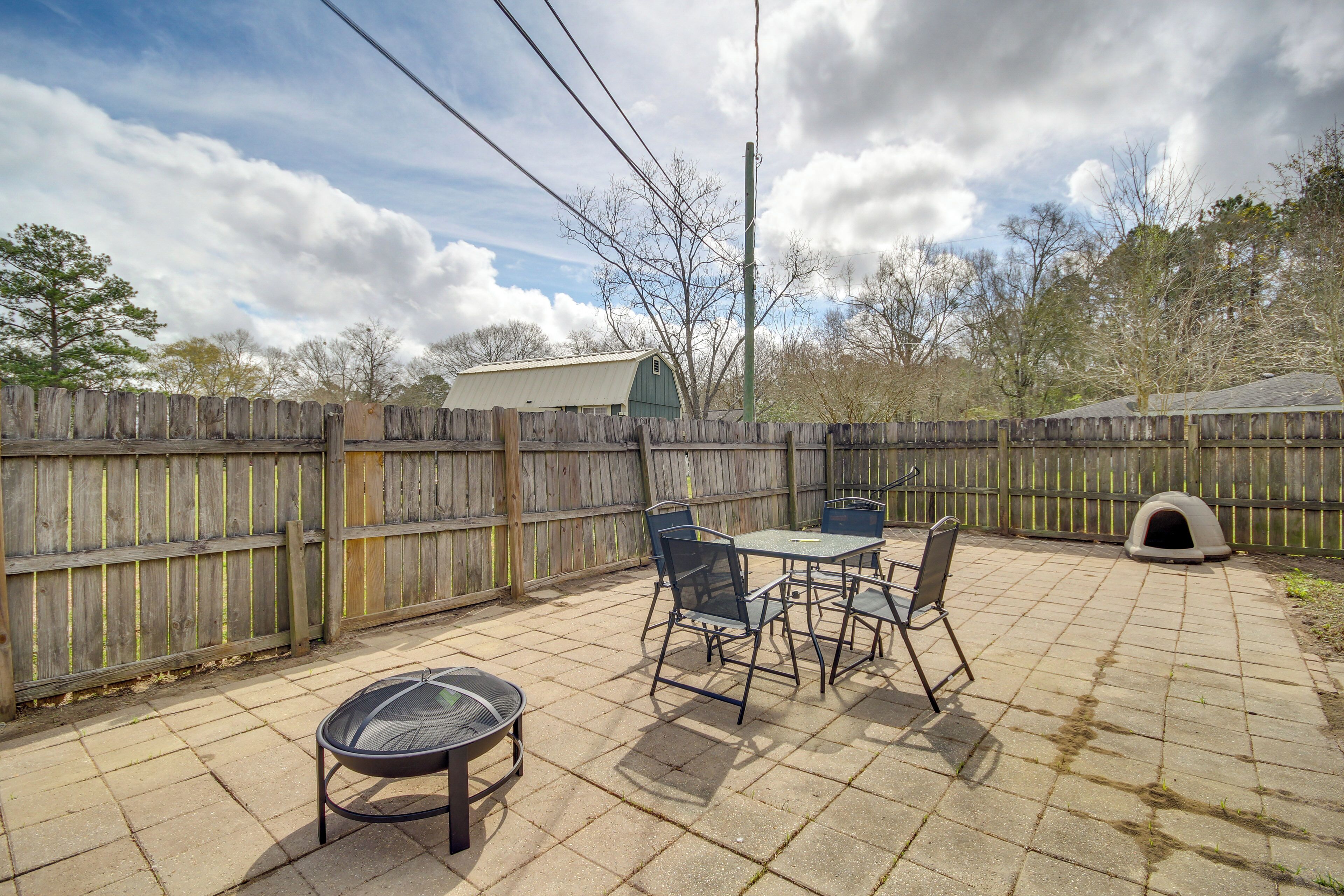 A patio with a table and chairs, a grill, and a dog house.