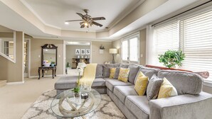 A living room with a gray sectional sofa, a glass coffee table, a ceiling fan, and a large window with blinds. - 7 Mi to Arthur Blank & Trilith Studios: Cozy Suite (Tyrone)