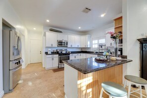 A modern kitchen with white cabinetry, a central island, stainless steel appliances, and a wooden accent wall. - Great Location & Free Extras! Bellflower Stay (Bellflower)