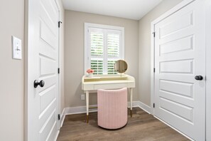 Um corredor com uma porta branca, uma toucador branco com um espelho, e um banquinho listrado em rosa.