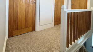 Un pasillo con puertas de madera, suelo alfombrado y baranda blanca.