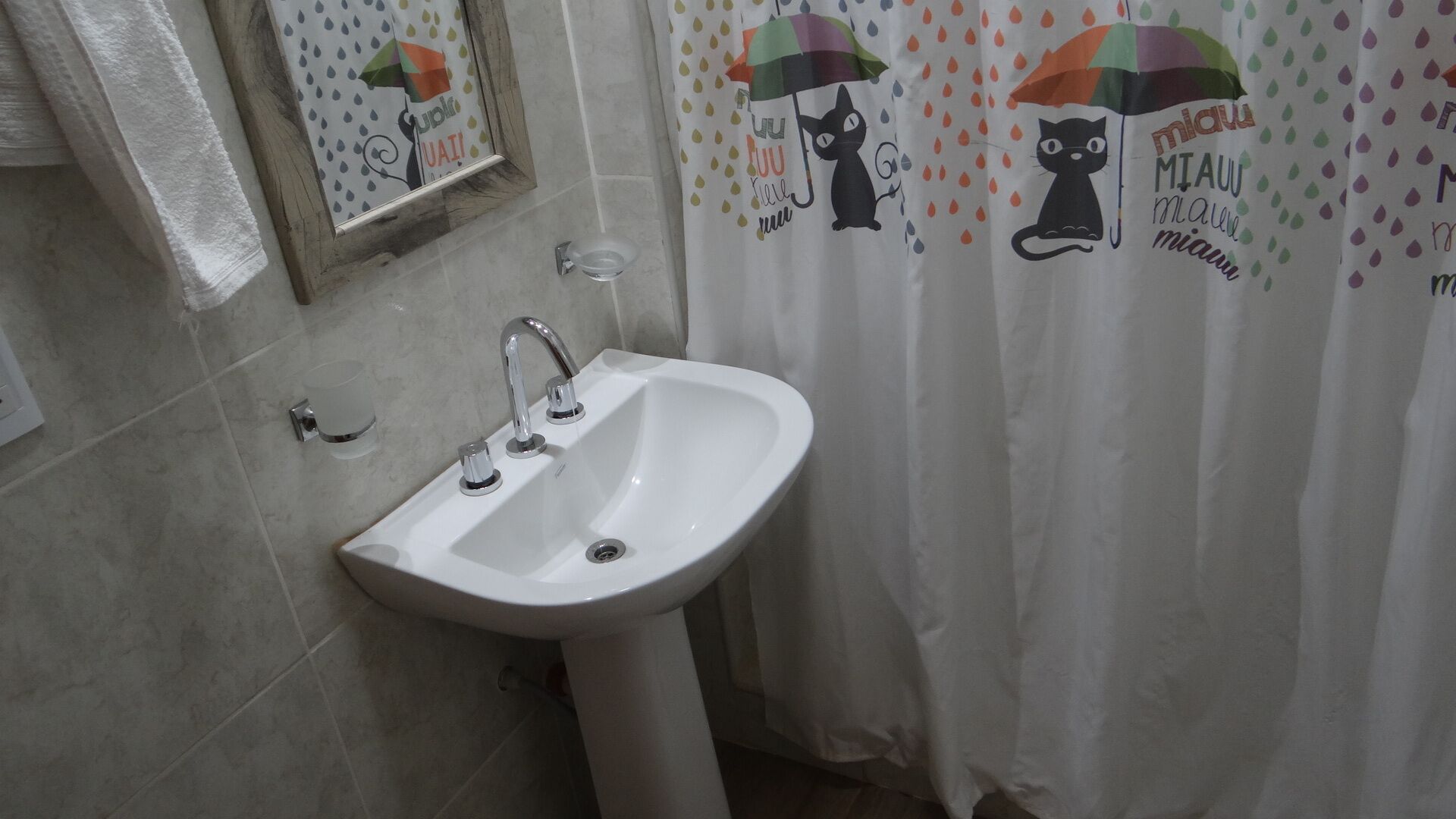 Ein Badezimmer mit einem weißen Waschbecken, einem Spiegel und einer Duschvorhang mit Katzenmotiven.