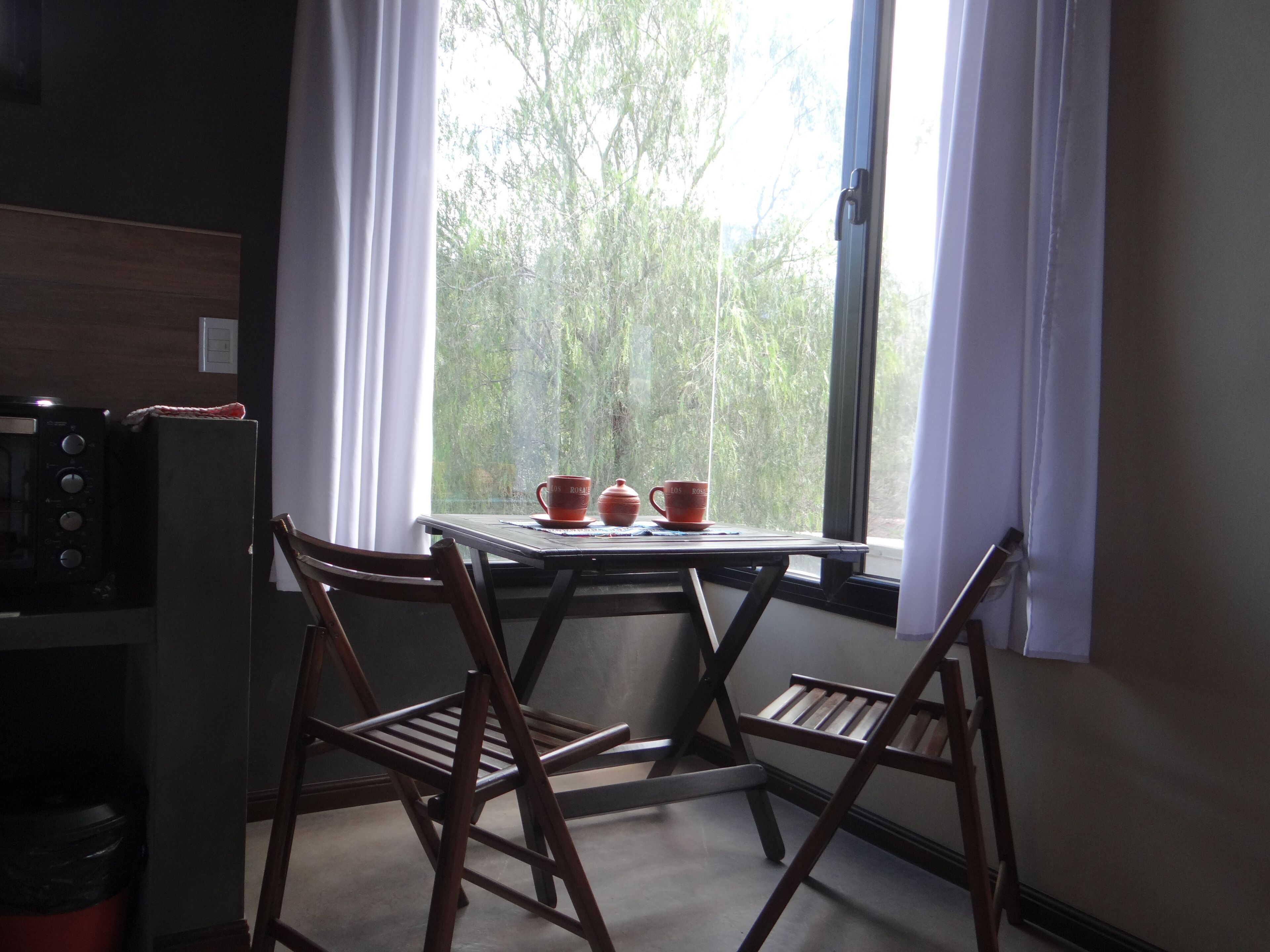 A room with a table by a window, two chairs, a microwave, and a trash bin.