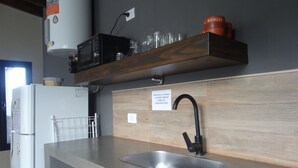 A kitchen with a built-in sink, a microwave, and a shelf with glassware.