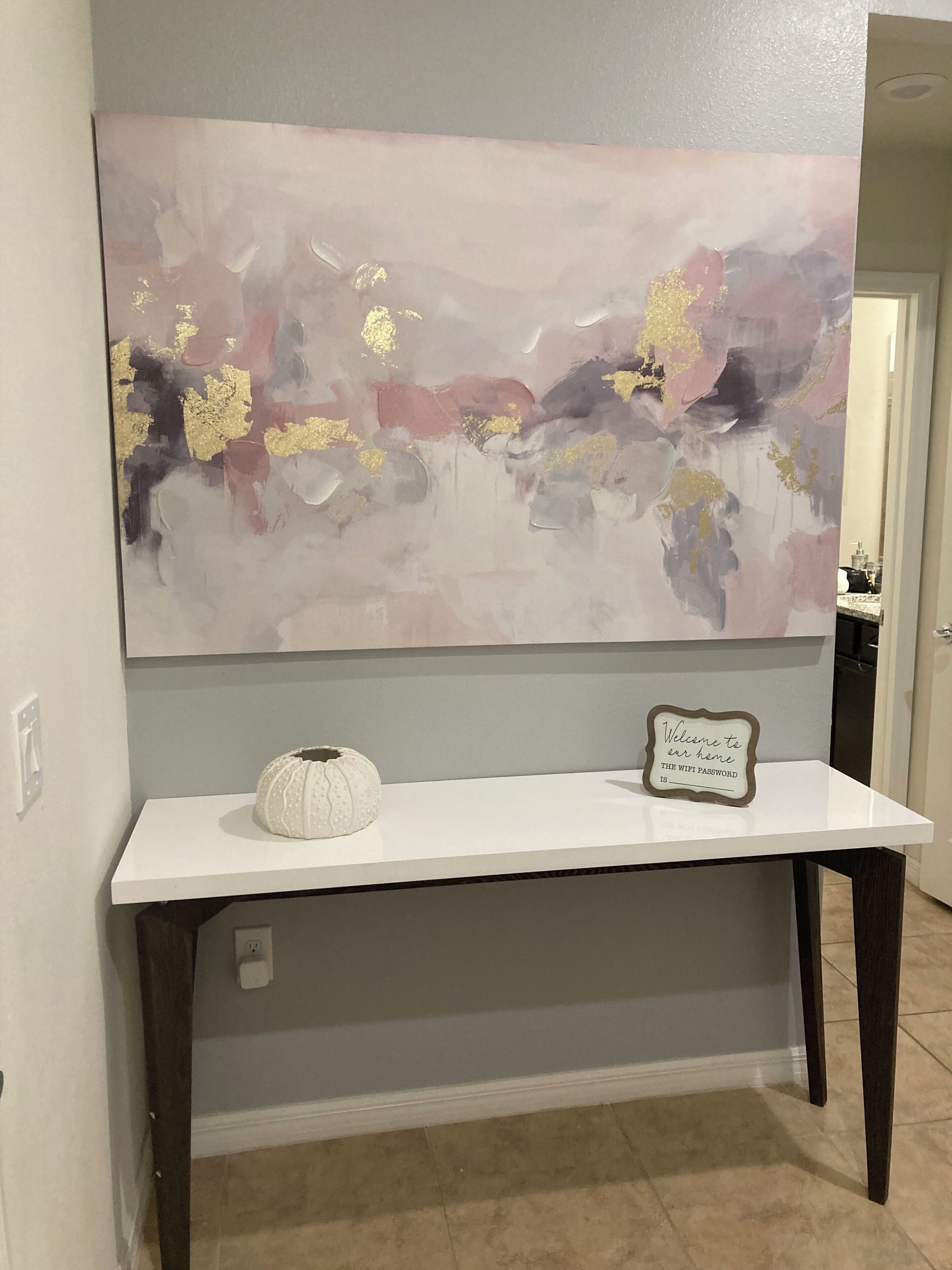 A room with a white console table, a decorative wall piece, and a sign with a Wi-Fi password.