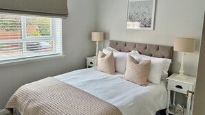 A bedroom with a bed, two bedside tables, a window with blinds, a ceiling lamp, and a wall-mounted picture. - The Kinfirth - cosy beach apartment (Ayr)