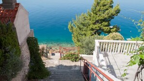 Un escalier menant à un balcon d’où l’on peut admirer une mer bleue et limpide, avec un arbre et une balustrade.