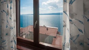 Une fenêtre donnant sur une mer calme et une terre lointaine, des rideaux à motifs bleus et une porte avec une poignée.
