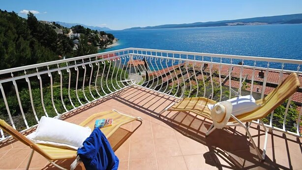 Un balcon avec deux chaises longues, un sol carrelé et une vue sur la mer et les collines lointaines.