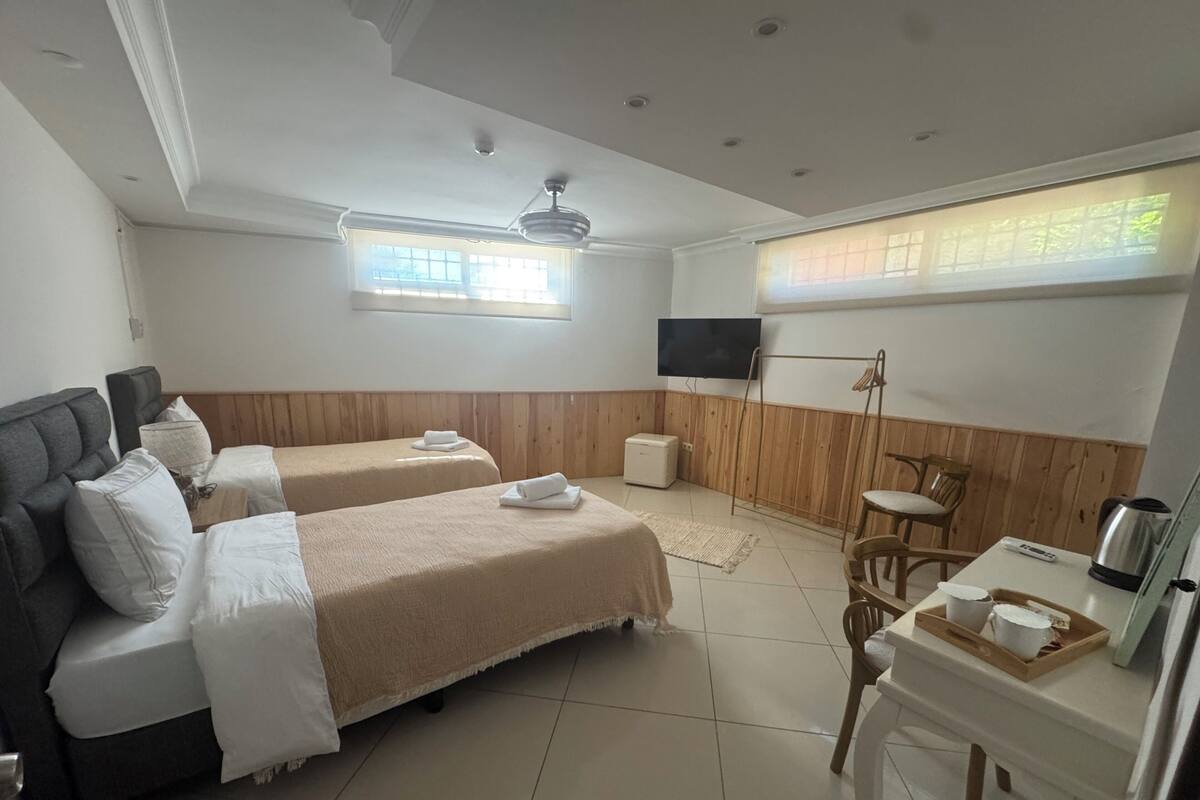 A hotel room with two beds, a TV, a desk with a kettle, and a window with a view.