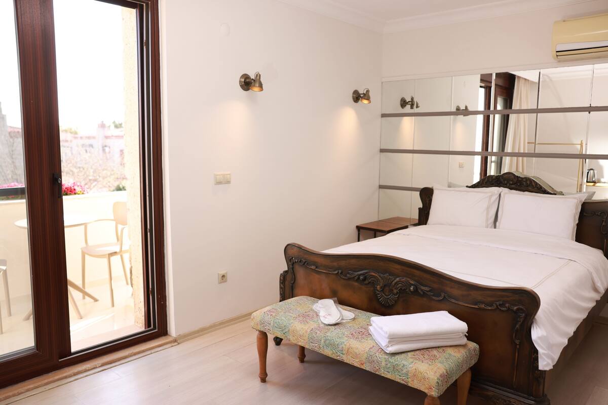 A bedroom with a large bed, a bench with towels, a bedside table, and a mirror.