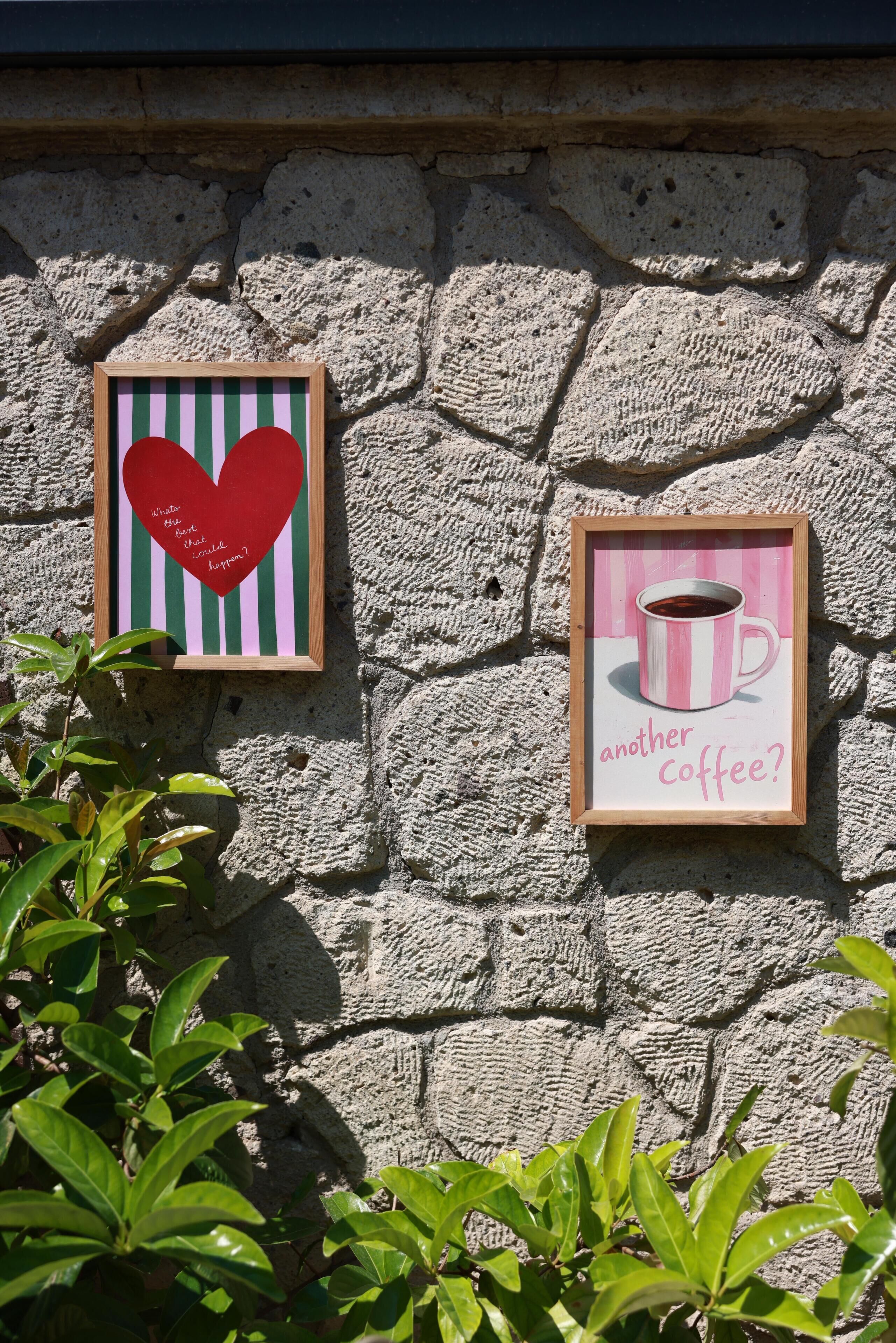 Dos cuadros enmarcados en una pared de piedra, uno con un corazón y texto, y otro con una taza de café y texto.
