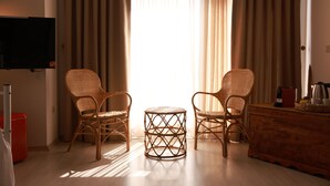 Une pièce comprenant deux fauteuils en osier, une petite table ronde, une commode en bois et un téléviseur fixé au mur.