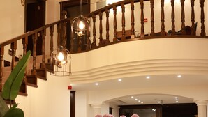 Un magnifique escalier en bois, doté d’une rampe et de luminaires suspendus, mène à un hall d’entrée bien éclairé où se trouve une table ronde ornée de fleurs et d’un vase.