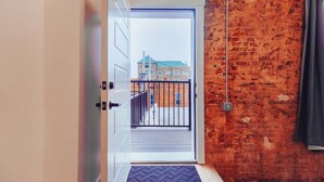 Une porte ouverte donnant sur un balcon d’où l’on peut admirer des immeubles et un mur de briques.
