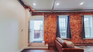 Une pièce avec un mur en briques, un canapé, une porte donnant sur un balcon et une fenêtre avec des rideaux.
