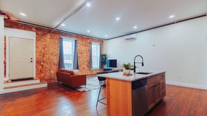 Une cuisine moderne avec un îlot central en bois, un lave-vaisselle encastré et un mur en briques.