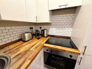 Una cocina con armarios blancos, encimera de madera, estufa negra, tostadora, hervidor y horno.