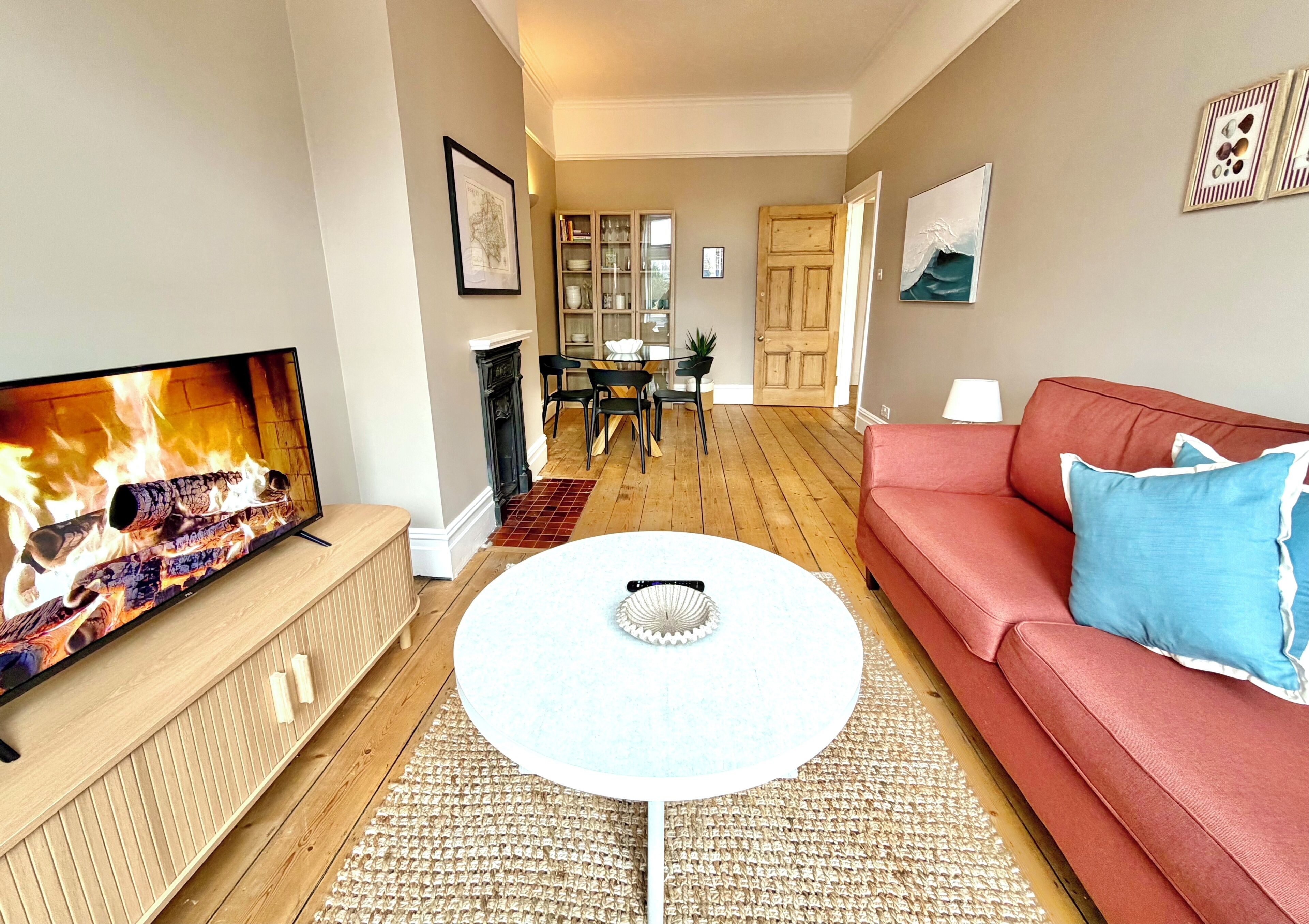 A living room with a TV, a red sofa, a round coffee table, and a dining area in the background.