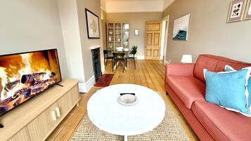 A living room with a TV, a red sofa, a round coffee table, and a dining area in the background.