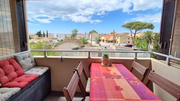 A balcony with a table and chairs, a cushioned bench, and a view of a residential area. - Saint Vincent near beach all comforts (le Grau D'Agde)
