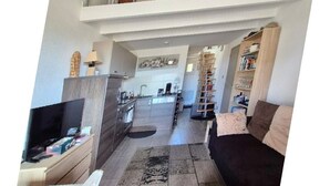 A spacious living area with a TV, sofa, and a staircase leading to an upper level. - Saint Vincent near beach all comforts (le Grau D'Agde)