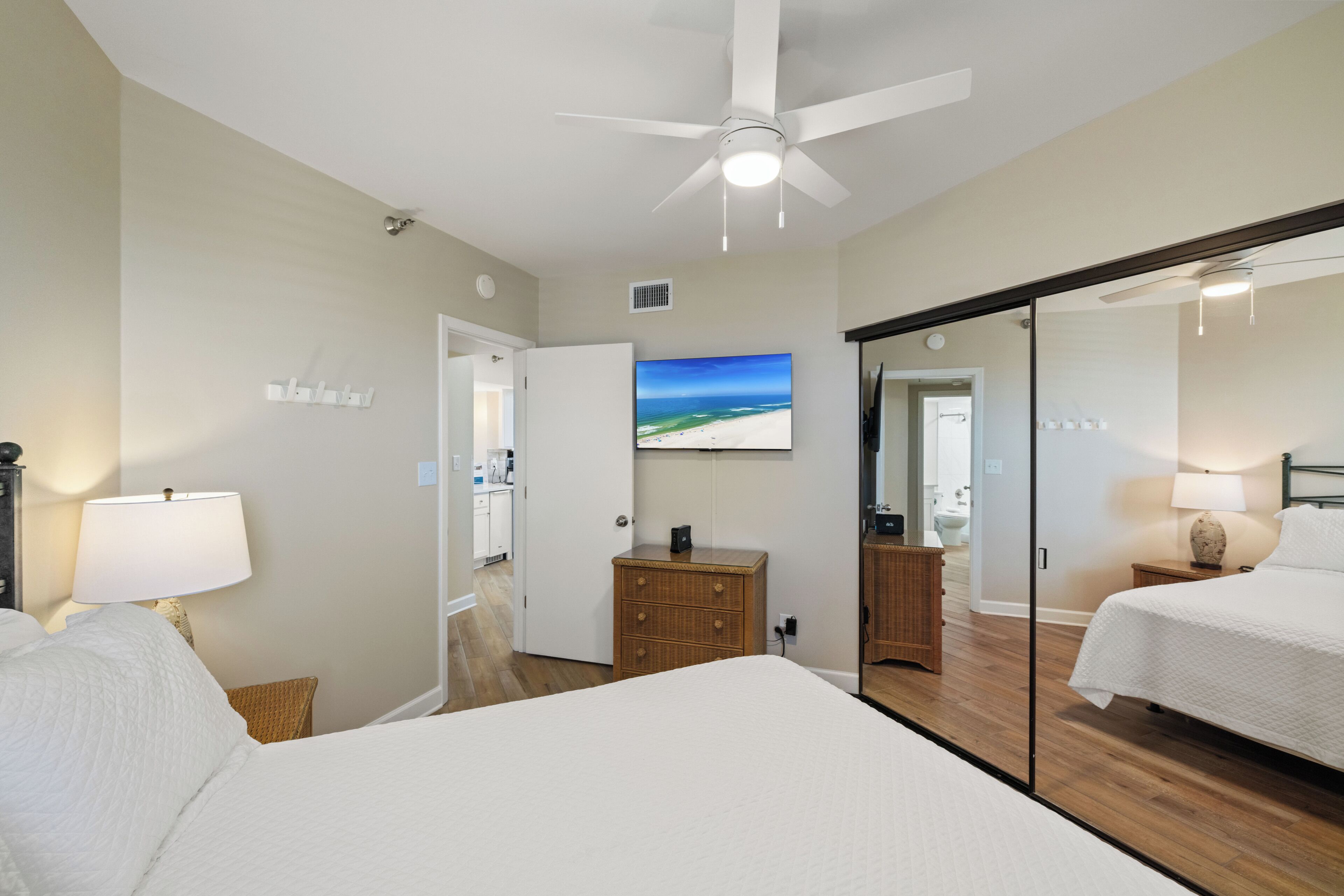 Ein Hotelzimmer mit einem Bett, einem Deckenventilator, einem an der Wand montierten Fernseher, einer Holzkommode und einem durch eine offene Tür einsehbaren Badezimmer.